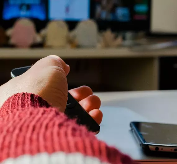 uma segurando um controle remoto enquanto assiste algum streaming